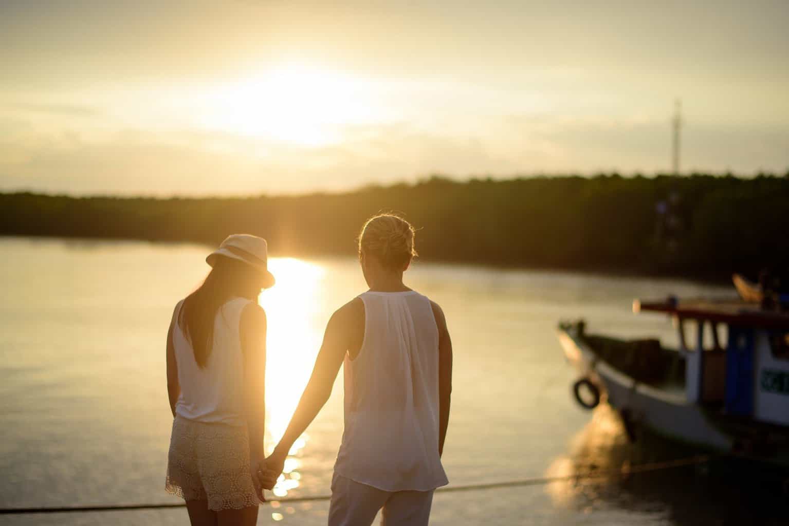 Frau und Mann stehen an einem See die Sonne geht unter und ein Boot ist zu sehen